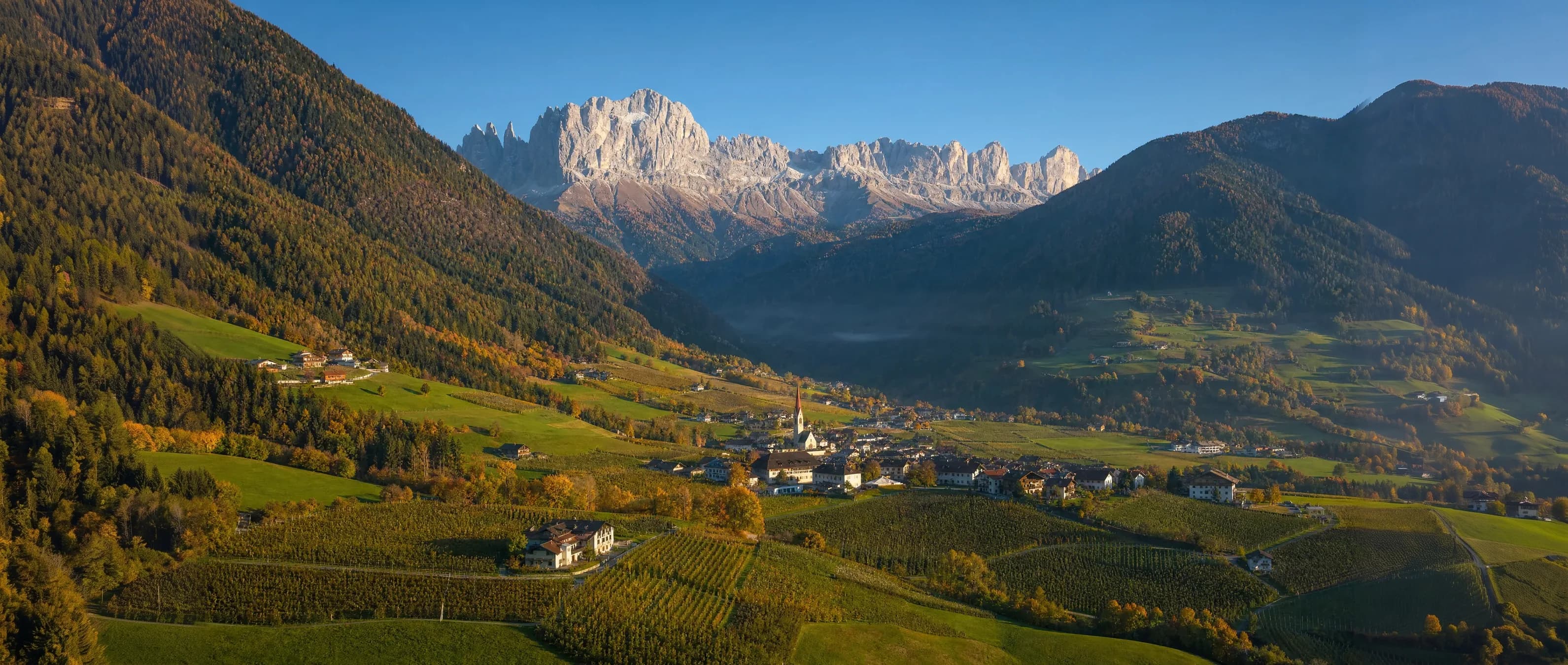 Südtiroler Tal mit Dorf, Apfelwiesen und den Dolomiten im Abendlicht